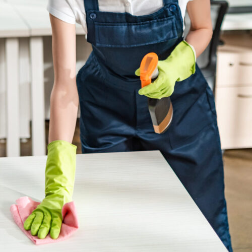 cheerful cleaner in overalls cleaning office desk with rag